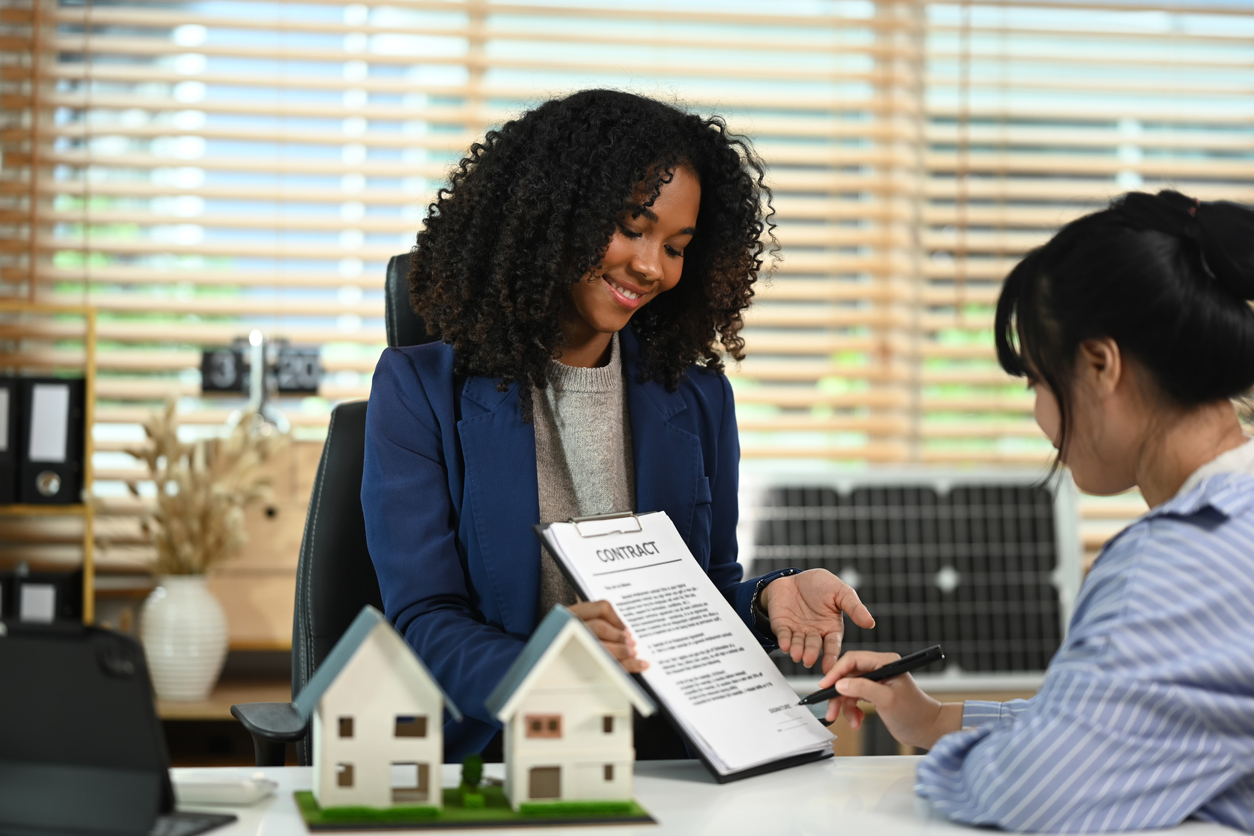 Professional real estate agent in suit pointing at contract document to client put a signature. Real estate and property insurance concepts.