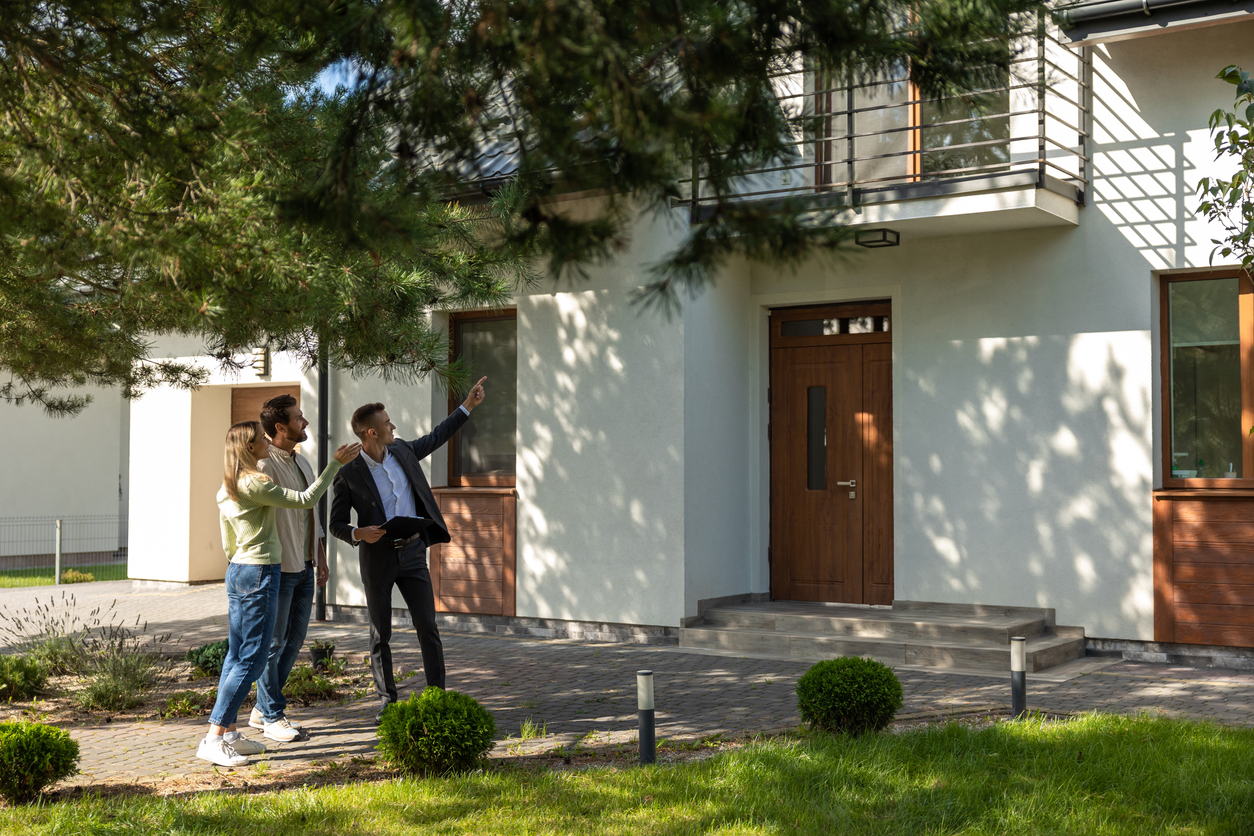 Agent showing house entrance to clients in suburban setting with clear sky